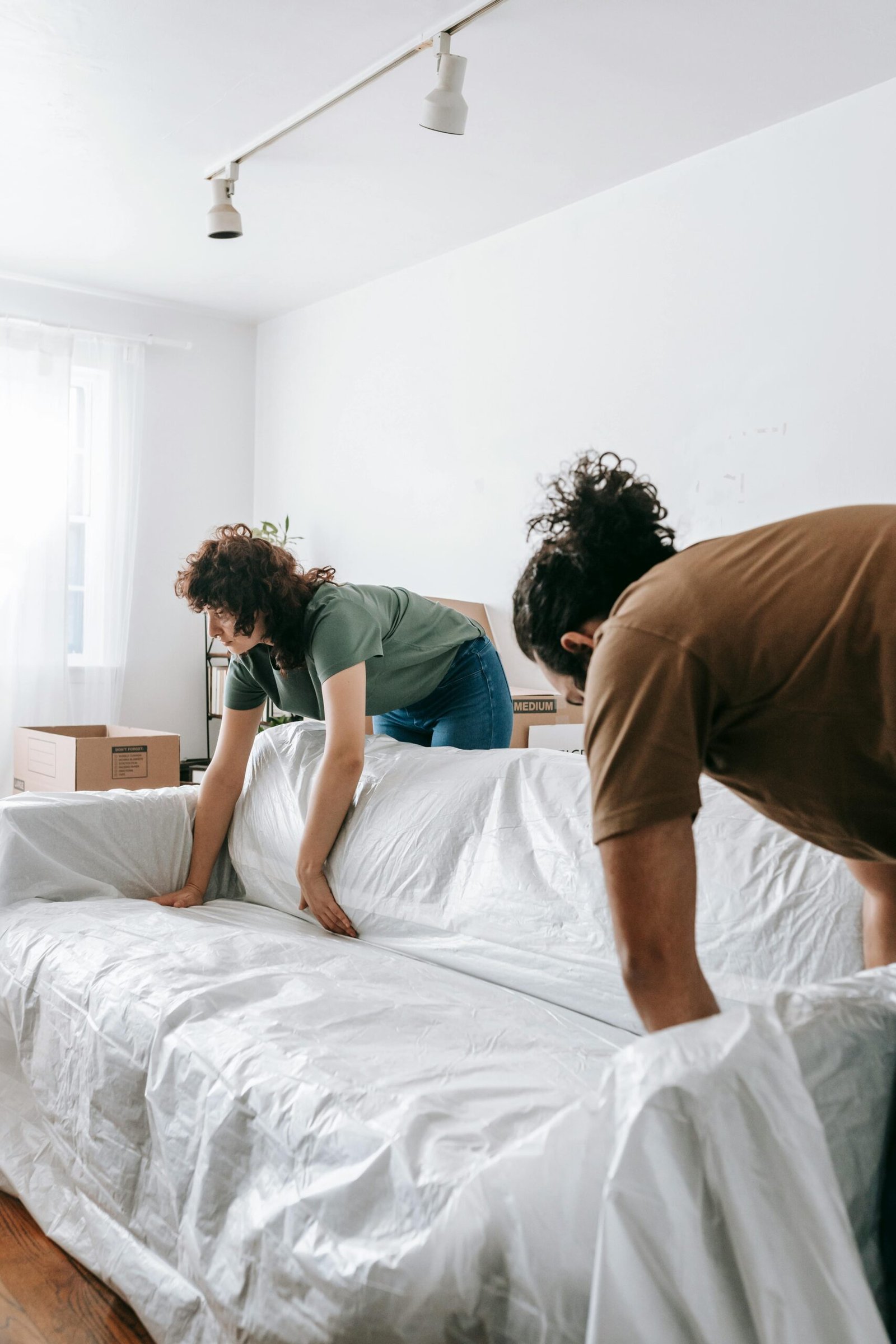 A couple packing their sofa for relocation by wrapping it in protective plastic.