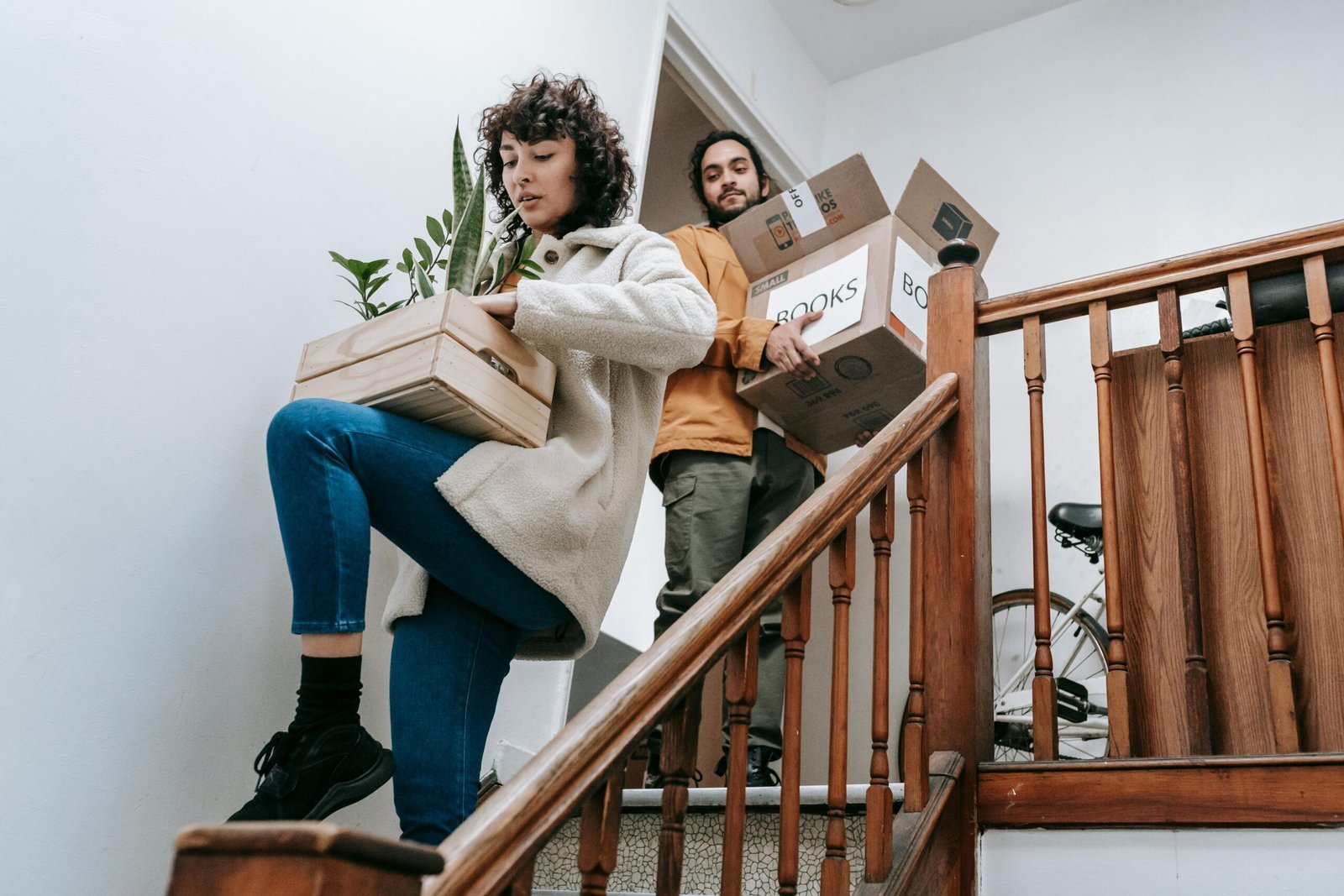 Couple carrying boxes and plants down stairs during a home move.