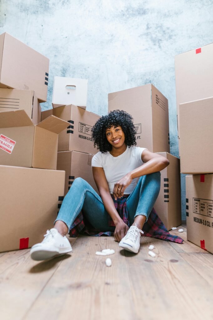 Smiling woman sitting with unpacked boxes during move-in day indoors.