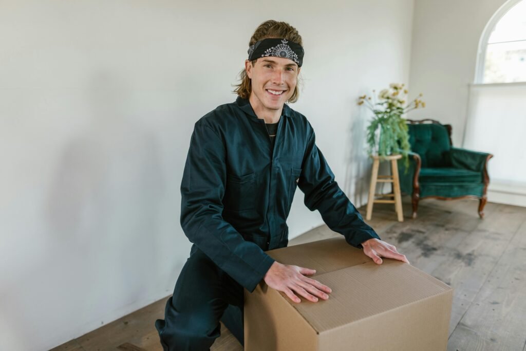 Young adult male smiling while handling a cardboard box indoors, preparing for moving day.